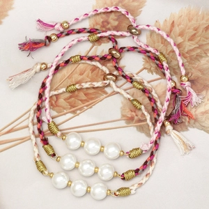 Detail of three handmade braided pearl bracelets with green and beige woven cords