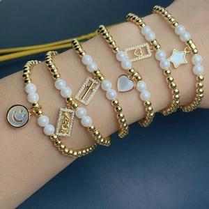 Macro shot of gold beads, white pearls, and varied pendants on stacked elastic bracelets