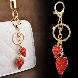 Golden strawberry keychain with red enamel fruit charms on a white quilted luxury bag