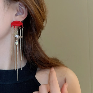 Close-up of red semicircular earrings with golden tassels and zircon butterfly details