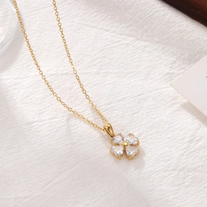 Elegant gold clover pendant necklace with clear zircon stones on white textured background