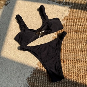 Detailed view of black bikini top with silver starfish metal buckle and ruched straps
