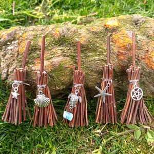 Detailed close-up of five mini witch brooms with various metal charms on natural grass