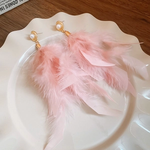 Macro shot of long pink feather earrings with white pearl detail on a white ceramic plate