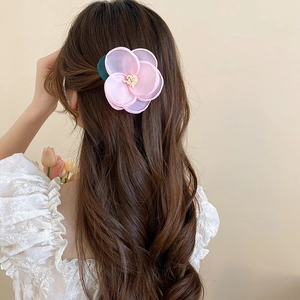 Detail of pink chiffon flower hair clip with green leaf on wavy brown hair