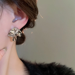 Macro detail of silver irregular flower earrings worn to show elegant metallic texture