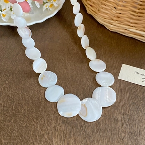 Elegant round shell necklace with natural iridescent gradient discs on a rustic wood table