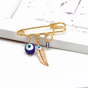 Detail view of a gold hamsa hand brooch featuring blue evil eye beads and a feather charm