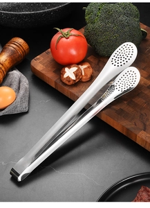 Détail de pince de cuisine en inox avec trous de drainage sur une planche en bois