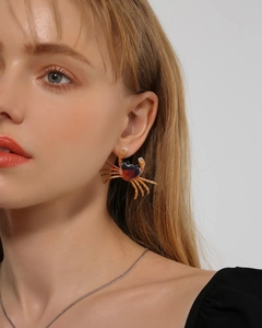 Primer plano detallado de pendientes de cangrejo 3D en naranja y negro sobre una modelo