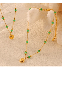 Close-up of gold shell pendant with green beaded chain on textured white background