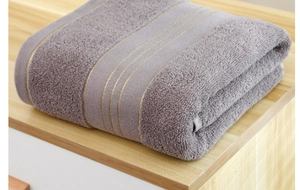 Close-up of thick cotton purple bath towel with golden stripe detail on wooden surface
