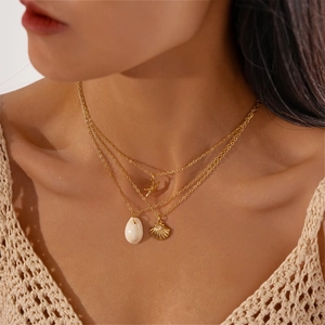 Detail of 3-piece gold layered necklace featuring seashell and starfish charms on a model