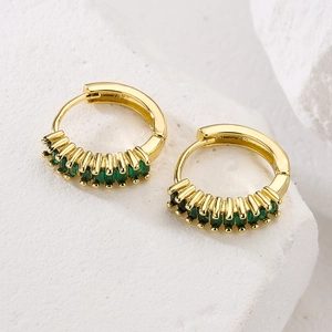 Gold hoop earrings with green rectangular zircon crystals on a white marble stone base