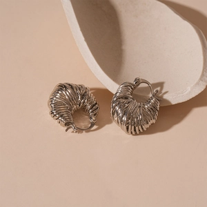 Macro shot of silver woven spiral hoop earrings on a textured minimalist background