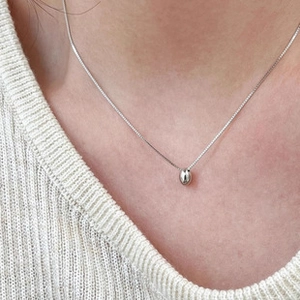 Close-up of minimalist silver bean pendant necklace worn on a white knitted sweater
