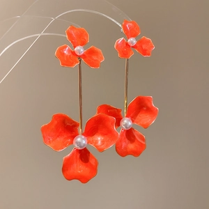 Detail of orange floral earrings featuring triple petals, pearl centers and gold links