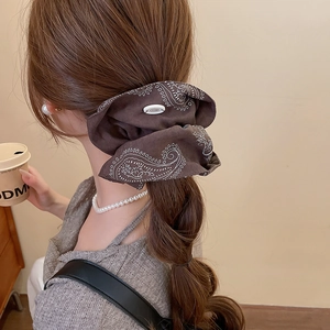 Close-up of a brown paisley print scrunchie with floral button on low ponytail hair