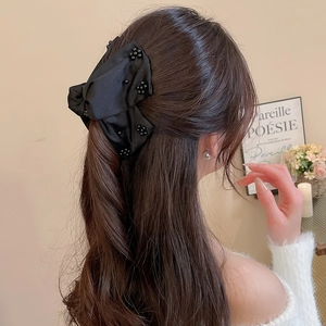 Detail view of a black satin bow hair claw with bead accents on a half-up hairstyle