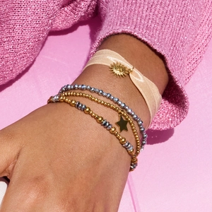 Punk style multi-layered gold and silver beaded bracelet with sun charm on pink background