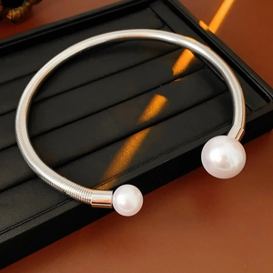 Close-up of silver metal open necklace with large white pearls on a black display tray