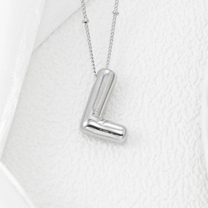 Detail macro of silver 3D bubble letter L pendant with high-polished mirror finish surface