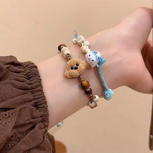 Detail view of handmade braided bracelets with ceramic cat and bear pendants on wrist