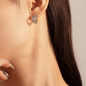 Macro shot of silver C-shaped geometric earrings with rhinestones on model's ear