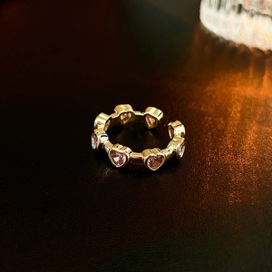 Close-up of gold plated ring featuring pink heart shaped zircon stones on dark leather