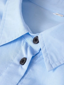 Detalle del cuello de la camisa azul claro con botones negros y costuras de alta calidad