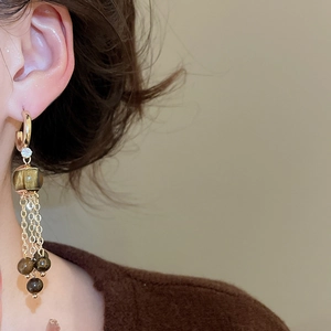 Detail of model wearing gold tassel earrings with tiger eye beads and zircon accents