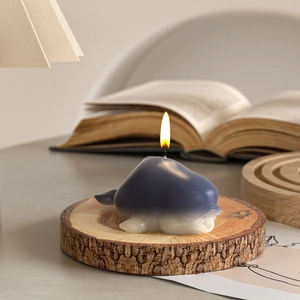 Close-up of a lit orca whale art candle on a rustic wooden slice with soft warm lighting