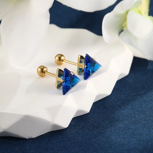 Detail of gold-plated triangle earrings with blue gemstones on white plate