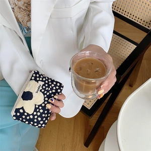 Detail of floral contrast drawstring makeup bag held with an iced coffee in a cafe