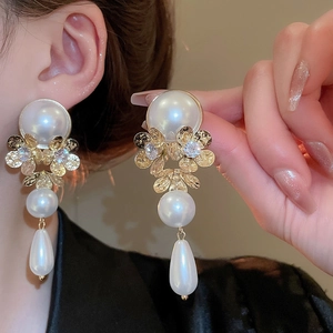 Macro shot of gold floral earrings with tassels and drop pearls on elegant model