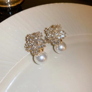 Macro shot of gold flower earrings with crystals and pearls on white ceramic plate