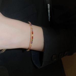 Detail of a thin gold cuff bracelet set with colorful rhinestones on a model wrist