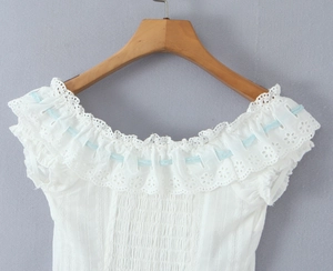 Detail of white lace embroidery top with light blue ribbon through the neckline eyelets