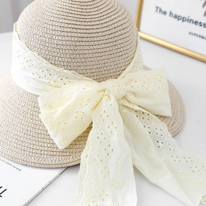 Close-up of summer straw hat featuring delicate lace bow and intricate floral embroidery