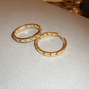 Detail of gold hoop earrings with colorful clover zircon stones on textured surface