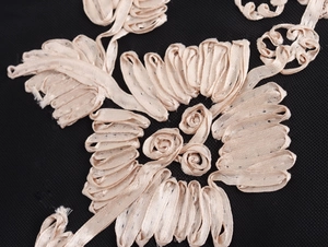 Detail van beige lintborduurwerk op de elegante zwarte mesh stof van de jurk