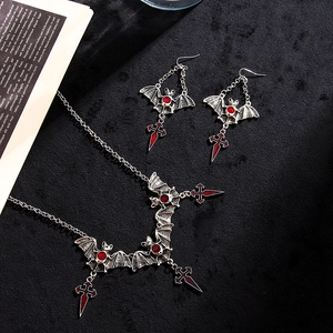 Macro shot of Gothic bat necklace and sword cross earrings with red gems on black velvet