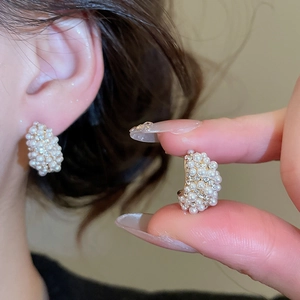 Detail of C-shaped gold hoop earrings featuring white pearls and sparkling zircons