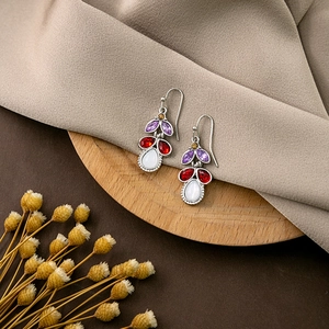 Detail shot of boho drop earrings with multi-color gems on a wooden tray with dried flowers