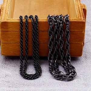 Detailed close-up of dark metallic rope and twist chain necklaces on a wooden box