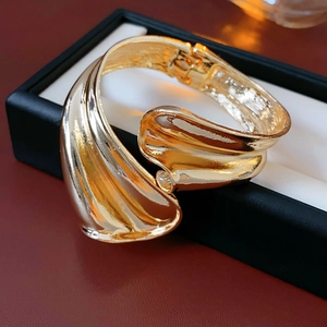 Macro detail of high-shine gold wide spiral bangle with irregular twisted metal wave design