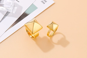 Detail showing two sizes of pyramid-style gold stainless steel rings on a pink background
