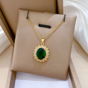 Primo piano della collana ovale dorata con gemma verde e diamanti su carta da gioielli