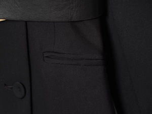 Dettaglio dell'abito blazer nero che mostra trama del tessuto, bottoni e cintura in pelle