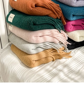 Close-up of stacked colorful knit scarves with handmade labels and soft fringe details